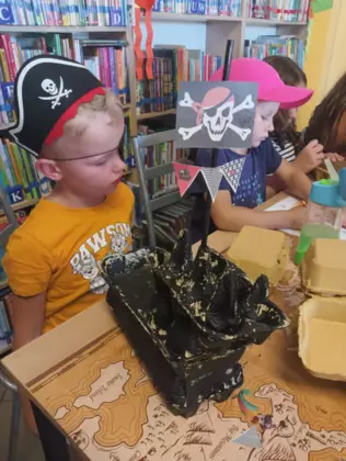 Statek piracki zrobiony z wytłaczanek po jajkach pomalowanych farbami. Obok stoi chłopczyk z czapką piracką na głowie i opaską na oku.