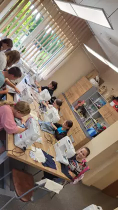 Dzieci siedzą przy stole przy maszynach i szyją torby.