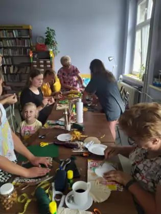 Uczestnicy warsztatów siedzą przy stole i wyczesują szczotką wełniane sznurki.