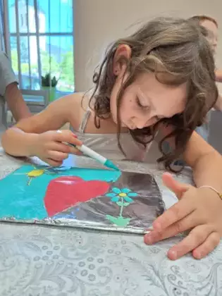 Dziewczynka koloruje na folii obrazek ukazujący kwiatek oraz słoneczko.