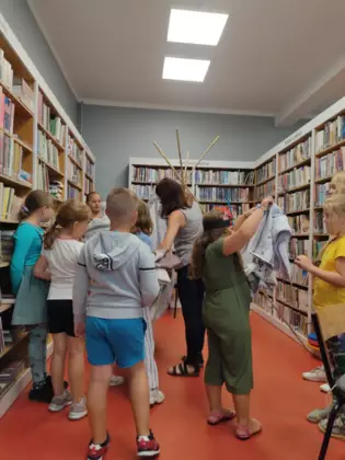 Dzieci wraz z panią bibliotekarką tworzą namiot tipi.