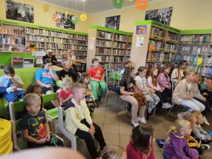 Widzowie spektaklu, dzieci siedzą na krzesełkach w bibliotece i oglądają przedstawienie.