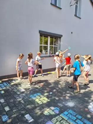 Dzieci puszczają bańki mydlane przed budynkiem biblioteki.