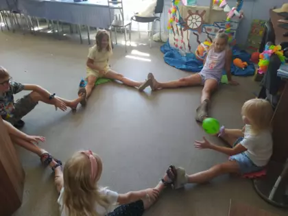 Dzieci siedzą na podłodze i wykonują ćwiczenia gimnastyczne.