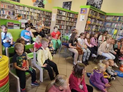 Widzowie spektaklu, dzieci siedzą na krzesełkach w bibliotece i oglądają przedstawienie.