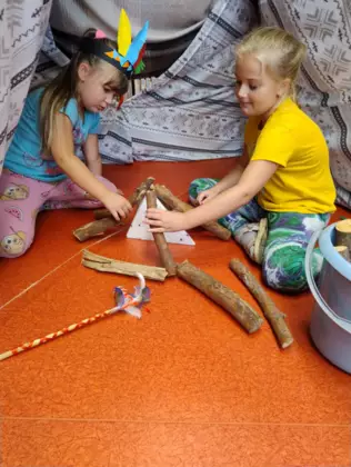 W namiocie tipi dziewczyny szykują drewno na ognisko.