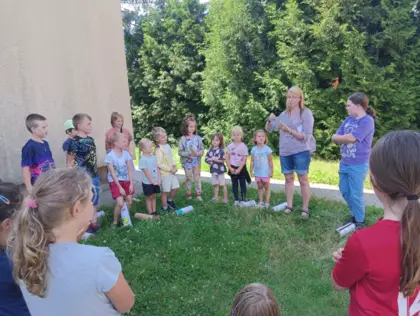 Dzieci zebrani w kole słuchają pani Małgosi opowiadającej o owadach.