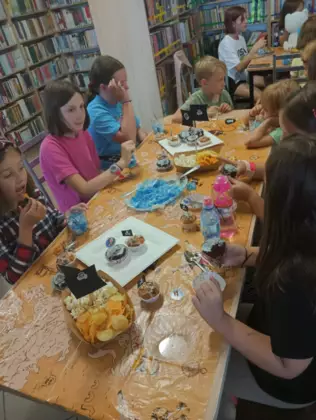 Dzieci częstują się babeczkami i chipsami.