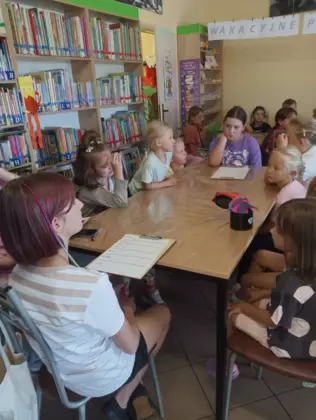 Dzieci siedzą w bibliotece przy stolikach i zapisują notatki odnośnie znalezionych owadów.