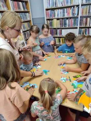 Uczestnicy zajęć wraz z panią instruktorką układają puzzle.