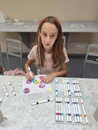 Dziewczynka mazakami maluje obrazki na ręczniku.