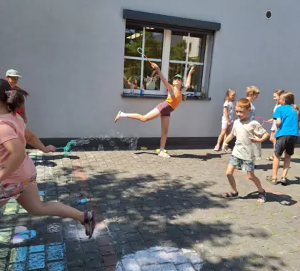 Dzieci puszczają bańki mydlane przed budynkiem biblioteki.