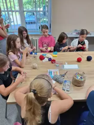 Uczestniczki siedzą przy stole i uczą się podstawowych splotów.