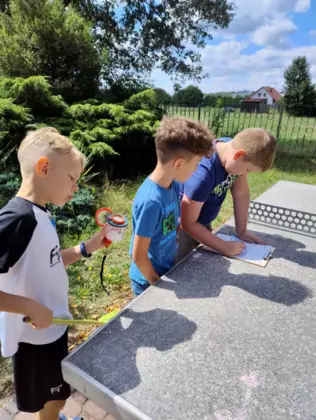 Chłopcy obserwują przez lupę owady i zapisują notatki na kartce.