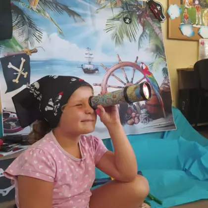 Dziewczynka w chuście pirata obserwuje przez lunetę mapę skarbów.
