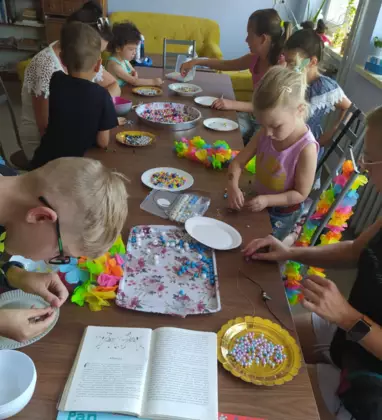 Uczestnicy zajęć siedzą przy stole i układają obrazki z koralików.