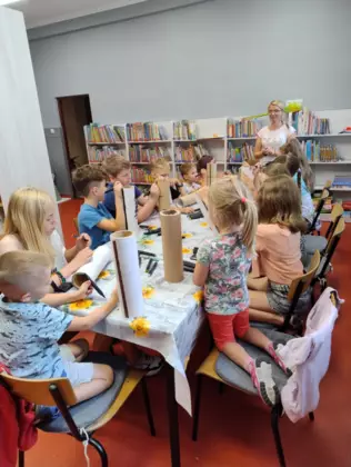 Dzieci siedzą przy stoliku i malują tekturowe tuby kolorowymi mazakami tworząc domki dla owadów.