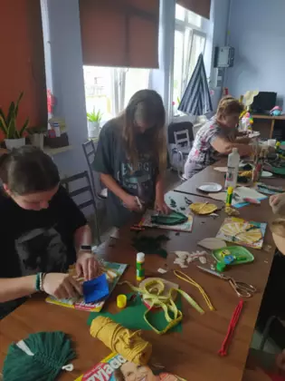 Uczestniczki wycinają sznurki, wyczesują oraz przyklejają listki do tekturki.