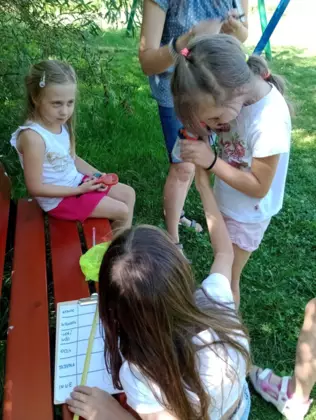 Dwie dziewczynki wnikliwiej obserwują przez lupę owada, którego złapały.