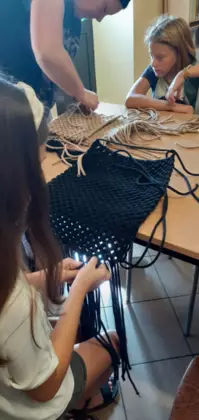 Dziewczyny wyplatają czarną i beżową torebkę.