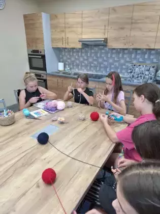 Uczestniczki siedzą przy stole i uczą się podstawowych splotów.