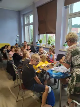 Uczestnicy zajęć siedzą przy wspólnym stole i szyją sówki.