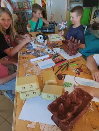 Dzieci siedzą przy stoliku i malują brązową farbą wytłaczanki po jajkach tworząc z nich statki.