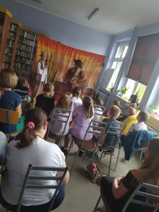 Dzieci ogladają przedstawienie siedząc na krzesełkach.