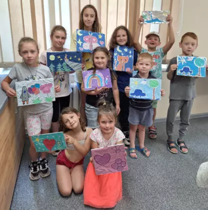 Wspólne zdjęcie dzieci po zajęciach literacko-plastycznych. Dzieci trzymają w rękach swoje obrazki, które namalowały na zajęciach.