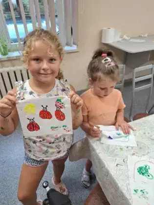 Dziewczynka trzyma w ręce ręcznik papierowy na którym narysowała biedronki.