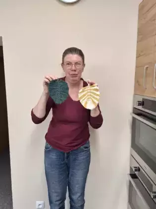 Uczestniczka zajęć pozuje do zdjęcia trzymając w rękach dwa liście wykonane na zajęciach.