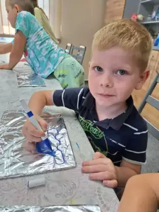 Chłopczyk maluje niebieskim mazakiem  samochodzik na folii aluminiowej.