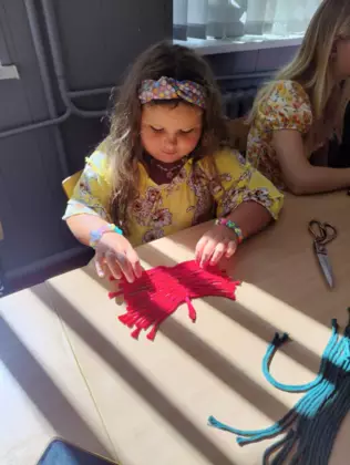 Dziewczynka wyczesuje listek makramy specjalną szczotką.