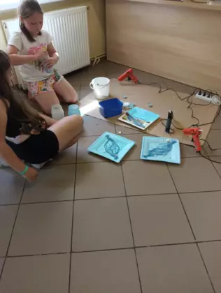 Dziewczyny kleją muszelki na pomalowane obrazki.