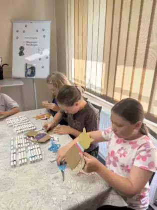 Dzieci owijają kartonowe kotki kolorową włóczką.