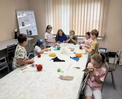 Dzieci owijają kartonowe kotki kolorową włóczką.