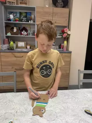 Chłopczyk owija kartonowego kotka kolorową włóczką.