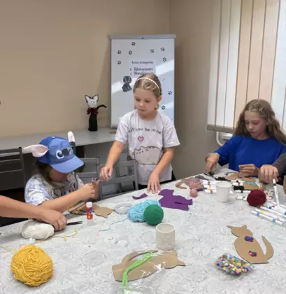 Dzieci owijają kartonowe kotki kolorową włóczką.