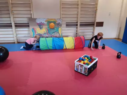 Sala sportowa, dzieci przechodzą przez kolorowy tunel. W pudełku na podłodze skrzynka z kolorowymi kuleczkami.