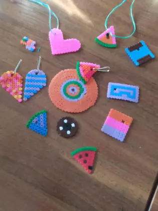 Na stole leżą kolorowe plastikowe breloczki w  kształcie serca, kawałka arbuza, trójkąta, kwadratu.