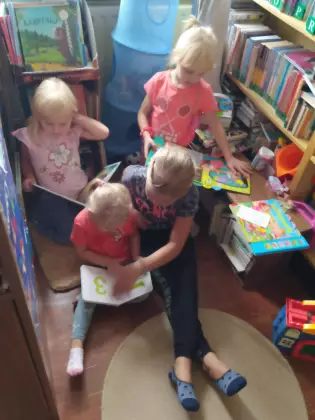 W bibliotece cztery kilkuletnie dziewczynki  siedzą na podłodze i czytają książki.