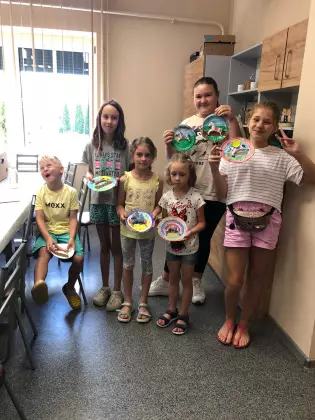 Kilka dzieci pozuje do zdjęcia, w rękach trzymają prace wykonane z talerzyków papierowych. Dzieci uśmiechają się.