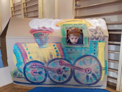 Na dużym kartonie namalowana kolorowa lokomotywa z wyciętym oknem. W oknie głowa kilkuletniego chłopca.