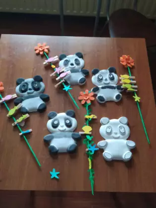 Na stole leżą pomalowane farbą gipsowe misie panda. Obok kolorowe kwiatki na patyku wykonane przez dzieci.