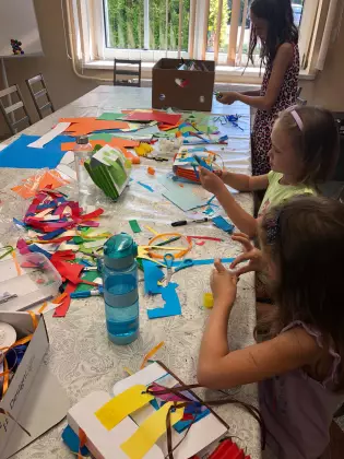 Na stole kolorowy papier pocięty na paski. Przy stole trójka dzieci wykonuje prace plastyczne.