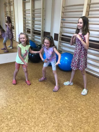 Trzy kilkuletnie dziewczynki stoją w pozie zamrożonej na hali sportowe. 