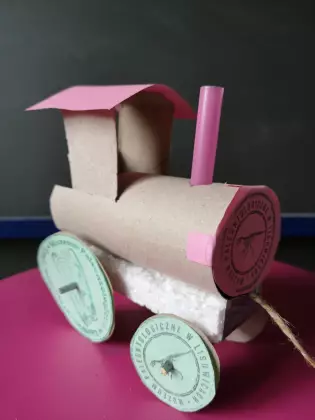 Na różowym blacie stoi lokomotywa z papieru z różowym daszkiem. 