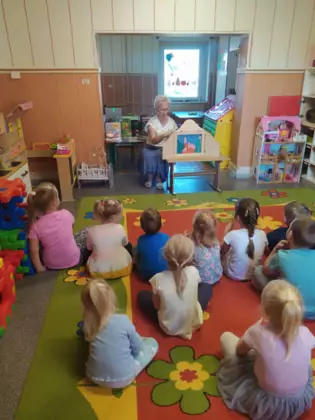 Przedszkolaki siedzą na dywanie i słuchają bajki.