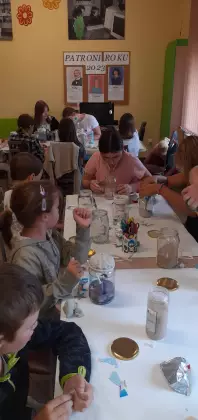 Uczestnicy siedzą przy stole i wykonują prace plastyczne.