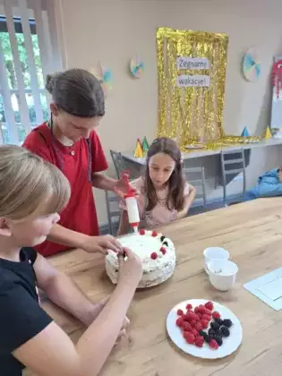 Dziewczyny dekorują tort owocami.